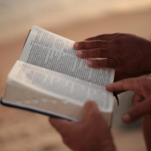 Close-up of hands holding an open Bible on a beach, symbolizing faith and study.