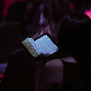 A young woman engrossed in reading a book while seated in a dimly lit room, captured in Jakarta.