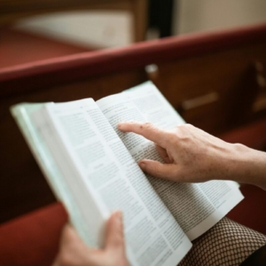 A close-up of hands holding an open Bible inside a church, symbolizing faith and devotion.