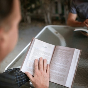 A man intently reading a Bible at an outdoor table, fostering a moment of spirituality and reflection.