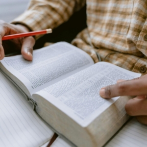 Hands holding an open Bible while taking notes with a pencil.